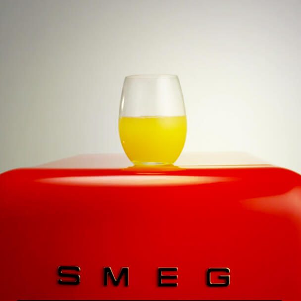 And glass with an orange drink on top of a red SMEG refrigerator.